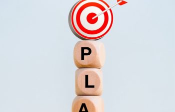 Business plan with goal and success concept. 3d target dart icon on wooden cube blocks stacked with text "PLAN" on wood table isolated on white background, minimalist, vertical style.